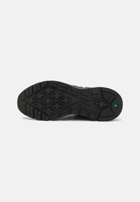 Semelle de chaussure en caoutchouc noir avec des rainures profondes et un accent vert. Le design comprend des motifs hexagonaux pour l'adhérence et la traction.