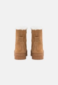 Braune Wildleder-Stiefeletten mit einem Kunstfellaufschlag, ausgestattet mit seitlichen Reißverschlüssen und gummierten Sohlen mit strukturierten Grip-Mustern.