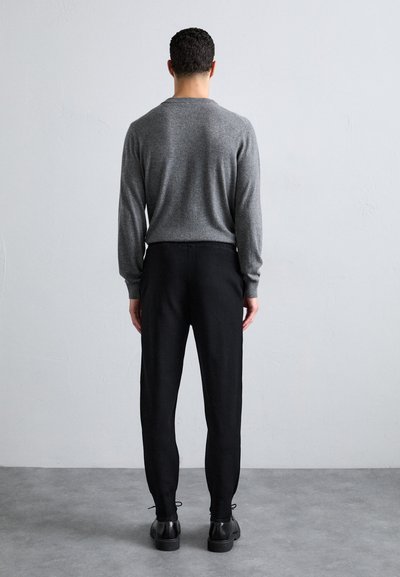 Grauer Strickpullover und schwarze tapered Hosen, kombiniert mit schwarzen Schnürschuhen. Einfaches Design, strukturiertes Wollmaterial und Details mit elastischem Bund.