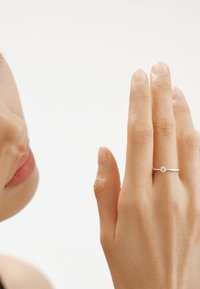 Anillo de plata con una sola piedra de diamante redonda, banda lisa, llevado en una mano con uñas naturales. El tono de piel es visible junto al anillo.