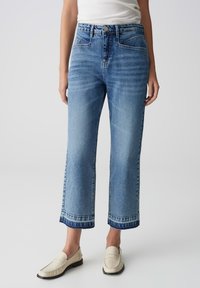 Jeans in denim azzurro chiaro con vestibilità dritta, vita alta e orlo grezzo. Presentano tasche frontali e una finitura sbiadita. Indossati con mocassini beige.