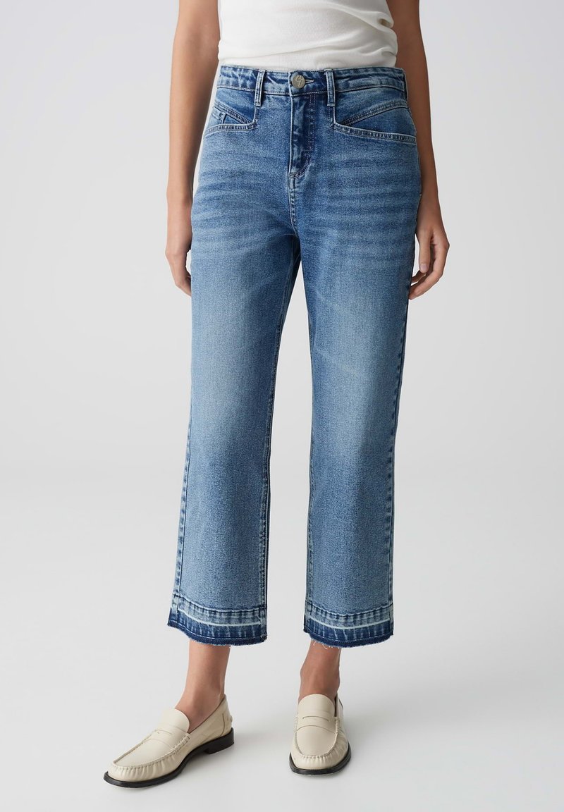 Jeans in denim azzurro chiaro con vestibilità dritta, vita alta e orlo grezzo. Presentano tasche frontali e una finitura sbiadita. Indossati con mocassini beige.