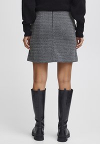 Jupe mini à carreaux gris avec une coupe droite et couture au dos, associée à des bottes en cuir noir jusqu'aux genoux avec des semelles épaisses.