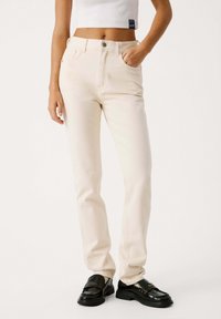 Jeans dritti color crema con alta vita, design a cinque tasche e dettagli di cucitura sottili, abbinati a mocassini neri.