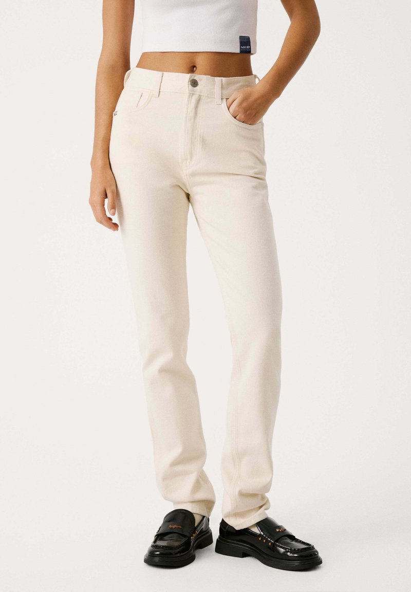 Jeans dritti color crema con alta vita, design a cinque tasche e dettagli di cucitura sottili, abbinati a mocassini neri.