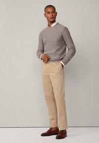 Harmaa neulepaita pyöreällä kaula-aukolla, beige chinot ja ruskeat nahkaiset loafersit. Sileä pinta, jossa hienovaraiset kuviolliset yksityiskohdat.