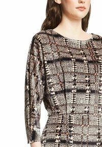 Knoopblouse in gemusterd stof met een combinatie van beige, zwart en perzik tinten. Geribbeld, met driekwart mouwen en een ronde halslijn.