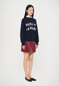 Marineblå ribbet sweater med hvid tekst, sat sammen med en burgunder faux læder nederdel. Sorte flade sko fuldender outfittet.