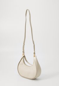 Borsa a spalla in pelle beige con forma curva, superficie testurizzata, dettagli in metallo dorato e tracolla regolabile.