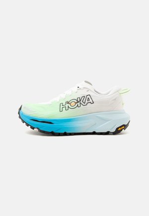 Chaussure de running Hoka blanche et bleue avec semelle épaisse et semelle extérieure Vibram noire, vue de côté montrant le grand logo HOKA sur la tige.