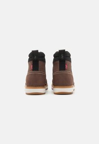 Botas de tobillo de ante marrón con cuello acolchado negro, entresuela blanca en contraste y suela de goma. Presentan lengüetas para tirar y detalles de costura.