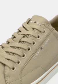 Baskets beige Tommy Hilfiger en toile, lacets beige et texte du logo blanc avec drapeau sur le côté et la languette.