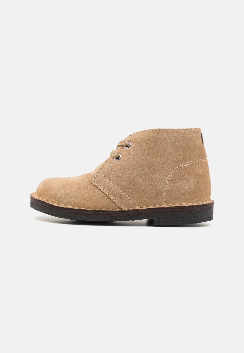 Botine din suede bej, cu vârf rotund, două găuri pentru șireturi, detalii cusute și talpă din cauciuc negru. Design minimalist cu textură netedă.