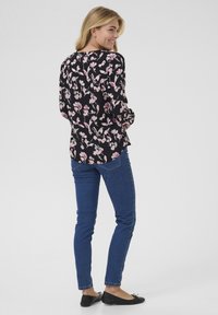Blusa a maniche lunghe con stampa floreale nera, decorata con fiori rosa e bianchi, abbinata a jeans skinny blu e ballerine nere. Tessuto morbido.