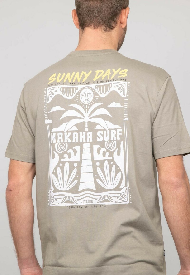 T-shirt vert olive avec un design imprimé blanc représentant un palmier, un soleil, et le texte "JOURS ENSOLEILLÉS" et "MAKAHA SURF" dans un style rétro.