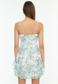 Blumenkleid mit weißem Grund, grün-blauem Blumenmuster, verstellbaren Spaghettiträgern, Rüschensaum und leichtem Stoff.