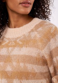 Suéter beige con cuello redondo, con rayas horizontales en tonos cálidos. Textura de punto con un acabado suave y ligeramente afelpado.