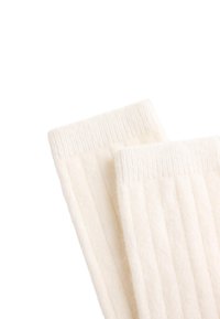 Ribbed hvide sokker lavet af blødt materiale, med en tyk tekstur og strikket kant, designet til komfort og varme.