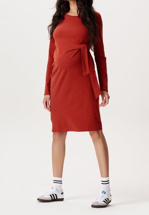 Ruosteenvärinen pitkähihainen mekko, jossa sivusolmu, valmistettu pehmeästä kankaasta. Yhdistetty valkoisiin kenkiin ja mustaraidallisiin sukkiin.