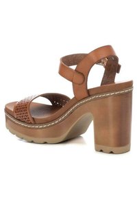 Sandalias de plataforma de cuero marrón con una tira de dedo perforada, correa ajustable en el tobillo y un tacón grueso. Plantilla texturizada y detalle de costura.