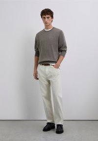 Ljust grå tröja med rund hals, kombinerad med off-white byxor med raka ben och svarta skor, som visar en minimalistisk design.