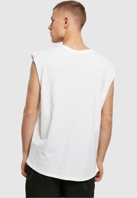 Hvid ærmeløs t-shirt med rund hals, glat tekstur og en afslappet pasform. Bagsiden viser skuldersømme og let buet kant.