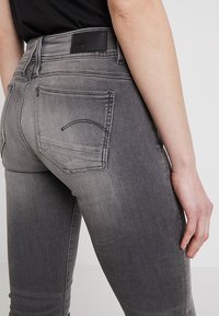 Grå denimjeans med en blekt finish, med en svart läderlapp vid midjan och bakfickans sömmar i en böjd design.