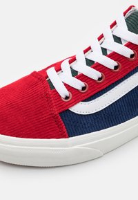 Zapatilla de pana en rojo y azul marino con cordones y detalles blancos. Presenta una distintiva franja lateral blanca y tejido texturizado. Suela de goma incluida.