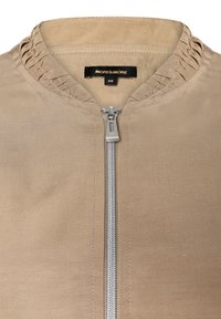 Beige Jacke mit strukturierter Kragen, silbernem Reißverschluss vorne und glatter Stoffoberfläche. Etikett lautet "MORE & MORE" in Größe 36.