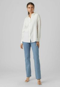 White button-up shirt with a textured finish, paired with light blue straight-leg jeans and white strappy heeled sandals.