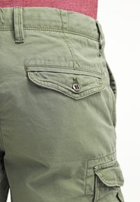 Olivově zelené cargo šortky s texturovanou tkaninou, několika kapsami a knoflíkovým detailem na zakřivené kapsičce.