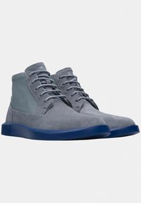 Stivaletti alla caviglia in suede grigio con una texture morbida, dotati di una suola in gomma blu e dettagli in tessuto grigio alla caviglia e ai lati.