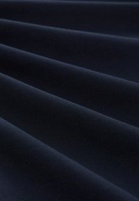 Ciemnoniebieska tkanina o teksturowanym splocie, z wieloma poziomymi fałdami, podkreślającymi jej gładką powierzchnię i głębię.