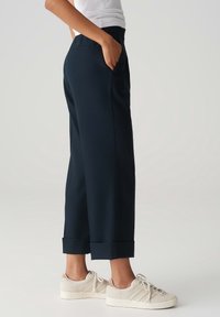 Pantalon bleu marine avec une coupe décontractée, doté d'une taille, de poches latérales et d'ourlets retroussés. Associé à des baskets de couleur claire.