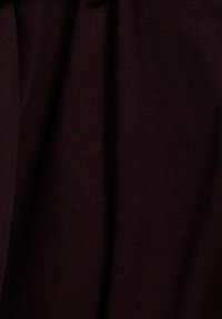 Gestructureerde stof in diep bordeaux met subtiele tonaal variaties, met een zachte breiconstructie. Geen merkbare patronen of accenten zichtbaar.