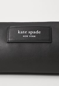 Black leather handbag featuring a rectangular logo patch with white text "kate spade NEW YORK." Smooth texture and simple design.