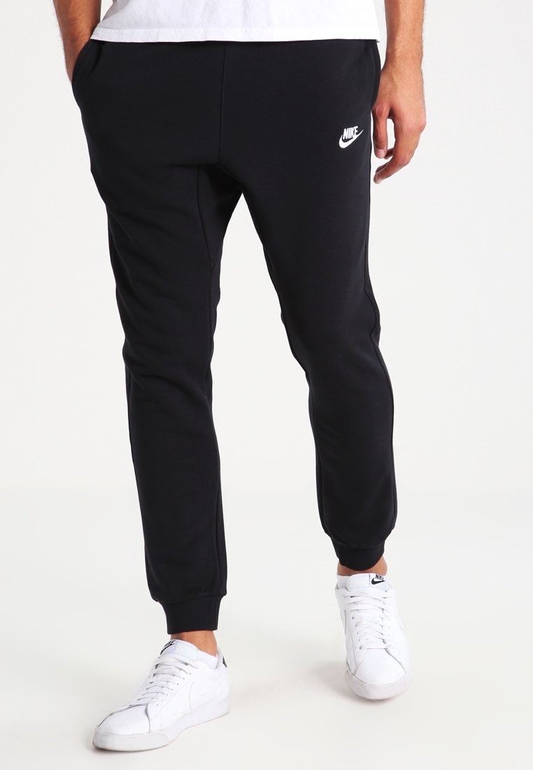 I pantaloni della tuta neri Nike presentano un design affusolato, una texture morbida, polsini elasticizzati e un accento di logo bianco sulla coscia sinistra. Indossati con scarpe da ginnastica bianche.