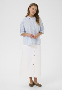 Blue and white striped button-up shirt with short sleeves, paired with a white midi skirt featuring front buttons and brown flat shoes.