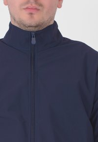 Mørkeblå zip-up jakke med høj krave, lavet af glat stof, med en central lynlås og en lille trækflap.