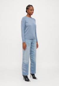 Svetlo modra pletena pulover s okroglim izrezom in rebrastim robom, združen z širokimi izrezanimi jeans hlačami iz blakonskega jeansa z diskretnim vzorcem, ter črnimi škornji s koničastim nosom.