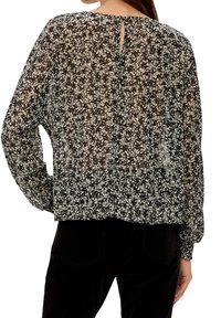 Schwarze transparente Bluse mit kleinen Blumenmustern, langen Ärmeln, abgerundetem Saum und einem Schlüssellochverschluss hinten mit einem Knopfdetail.