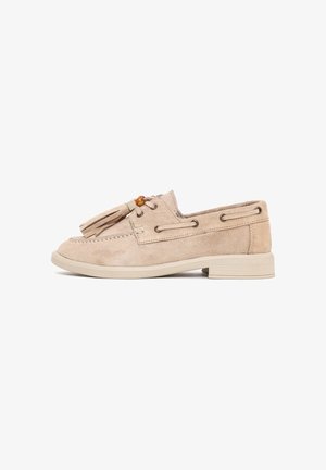 Beige suède loafer met kwastjes, houten kraalaccent, gestikte details en lage blokhak op witte achtergrond.