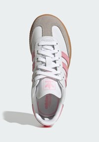 Biela kožená teniska s ružovými semišovými detailmi a tromi ružovými pruhmi. Má gumovú podrážku a jednoduché biele šnúrky.