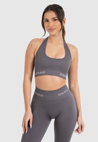 Sujetador deportivo gris y leggings a juego con textura acanalada; las bandas presentan el logo "SMIL"; diseño de cuello halter, silueta ajustada.