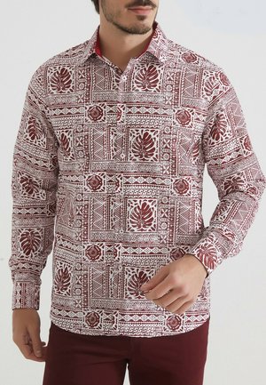 Chemise à manches longues blanche avec motifs géométriques et floraux rouges. Dotée d'un col intérieur et de poignets rouges, en tissu léger.