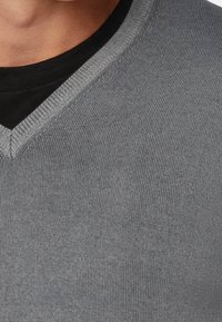 Šedý pletený svetr s výstřihem do V. Má texturovanou tkaninu a žebrovaný výstřih, vrstvený přes černé tričko.