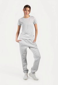 Hellgraues Baumwoll-T-Shirt und passende Jogginghose mit lockerem Schnitt, Bündchen an den Knöcheln und minimalen Details, kombiniert mit weißen Turnschuhen.