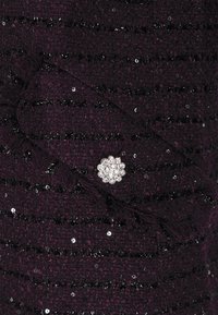 Material texturat de culoare mov cu sclipici și margini desfăcute, având o broșă florală argintie cu pietre transparente ca accent remarcabil.