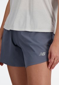 Graue Sportshorts aus perforiertem Stoff mit reflektierendem New Balance Logo. Das Material scheint leicht und flexibel zu sein, ideal für den Sport.