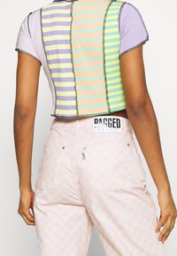 Cropped, multicolored ribbed top with pastel stripes and contrast stitching, paired with pink checkerboard denim pants featuring label at waist.